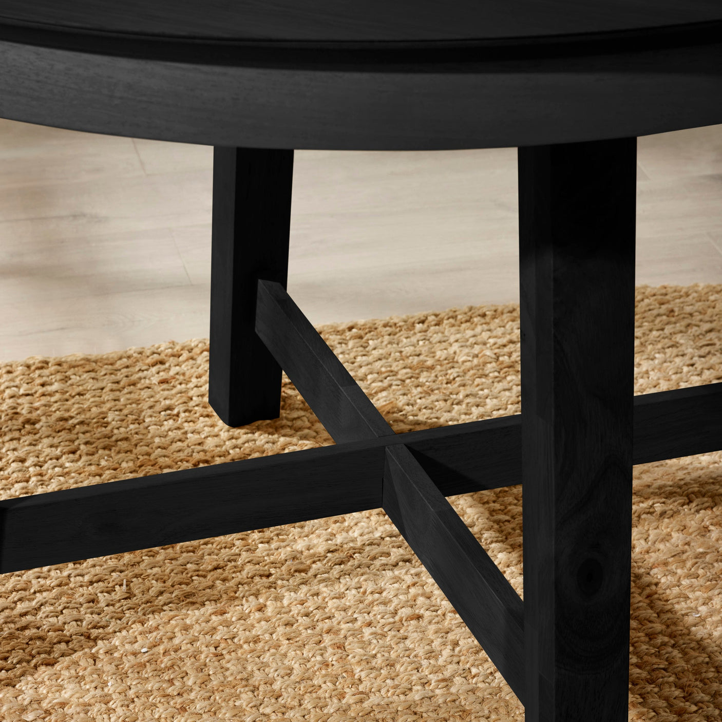 Close-up of black wooden dining table legs with cross support on woven natural fiber rug