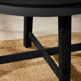 Close-up of black wooden dining table legs with cross support on woven natural fiber rug
