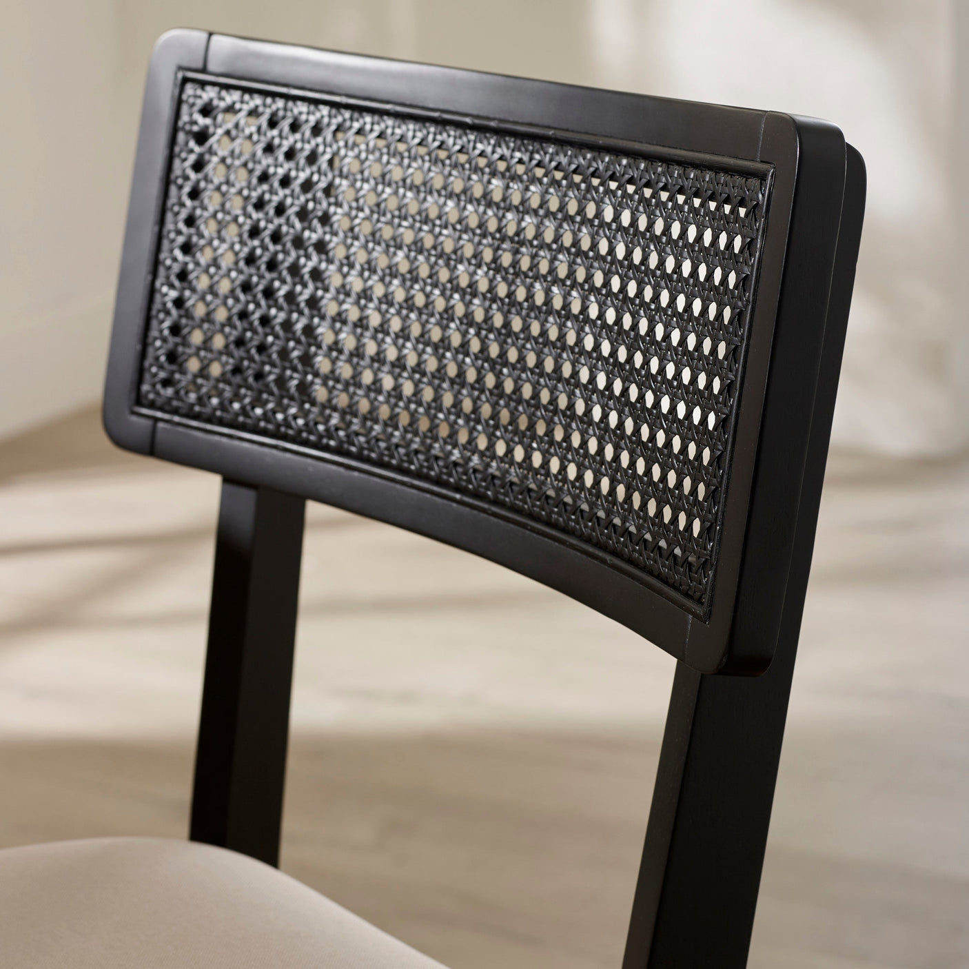 Close-up of black-framed rattan woven backrest of dining chair in light room setting