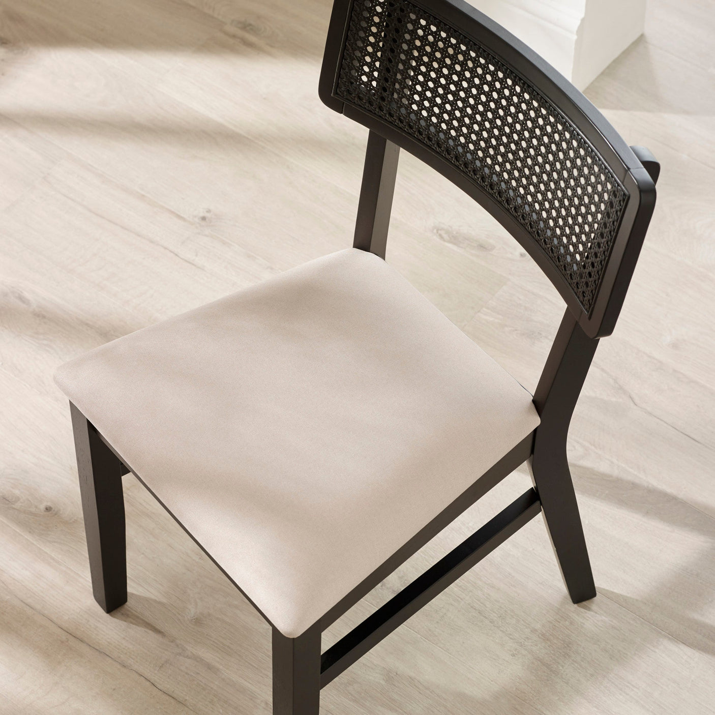 Top view of black dining chair with beige natural fabric seat and rattan backrest on light wood floor