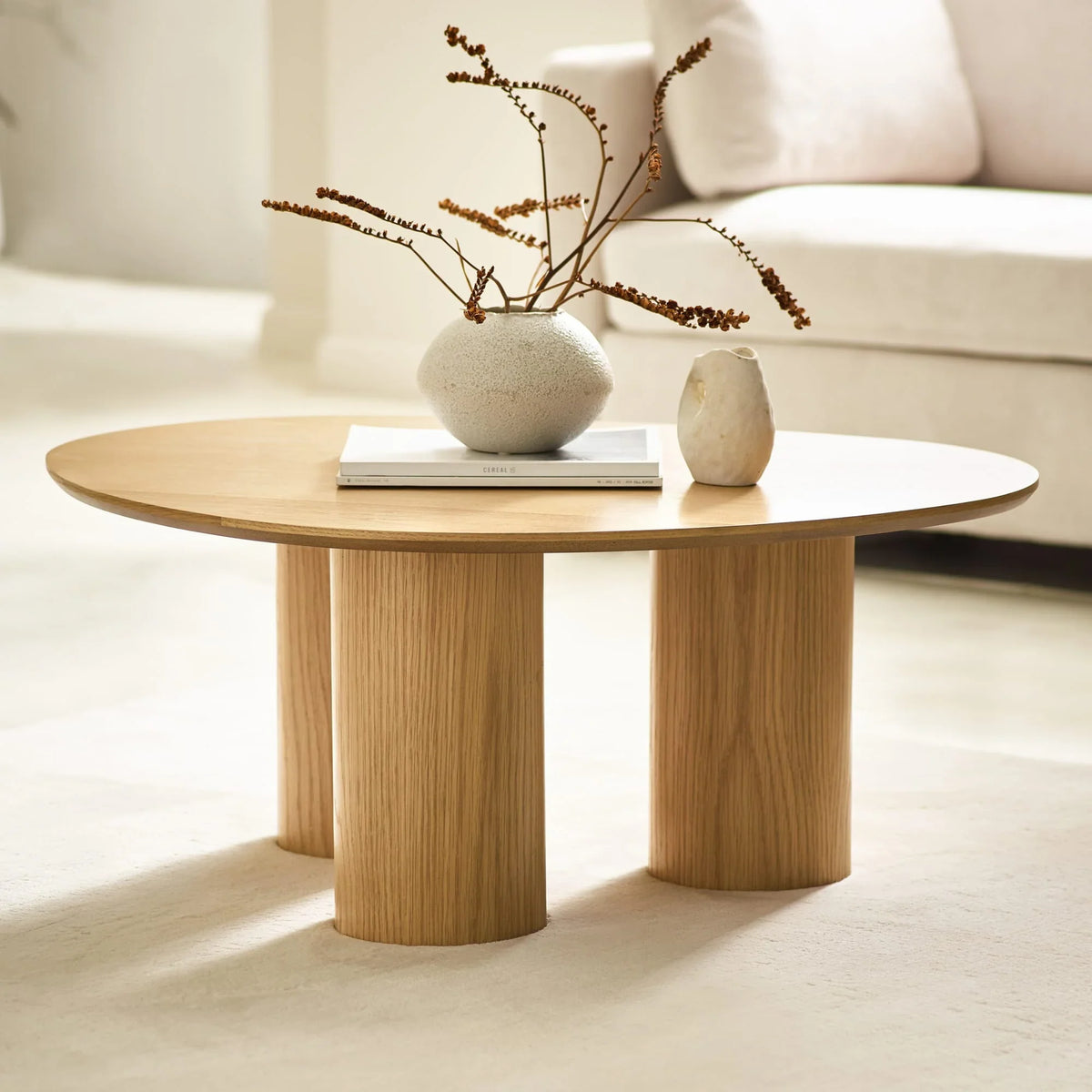 Round oak coffee table with three pillar legs, ceramic vases and books in living room