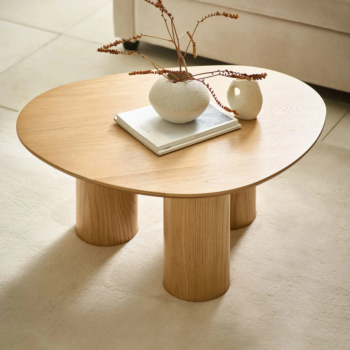 Oak coffee table with round top and three cylindrical legs, styled with books and vases