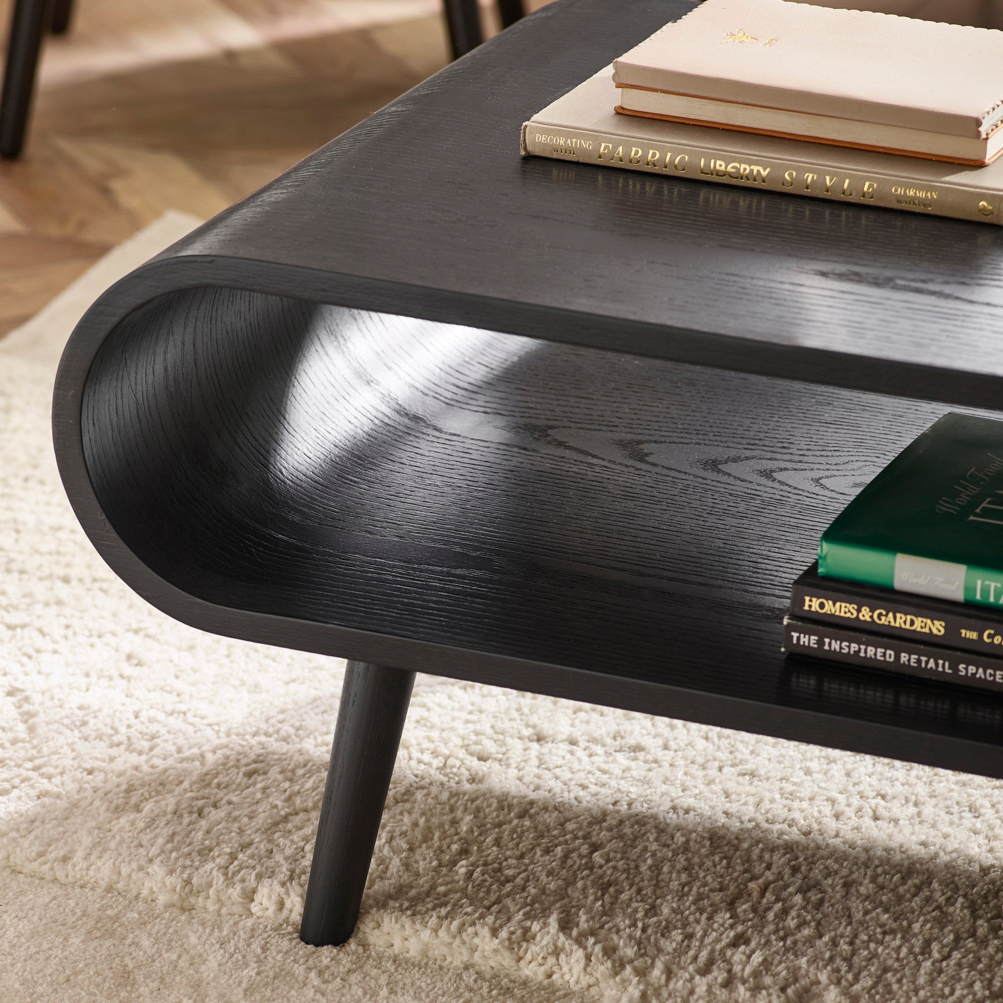 Close-up angled view of tapered leg and curved side of black wooden coffee table on light rug