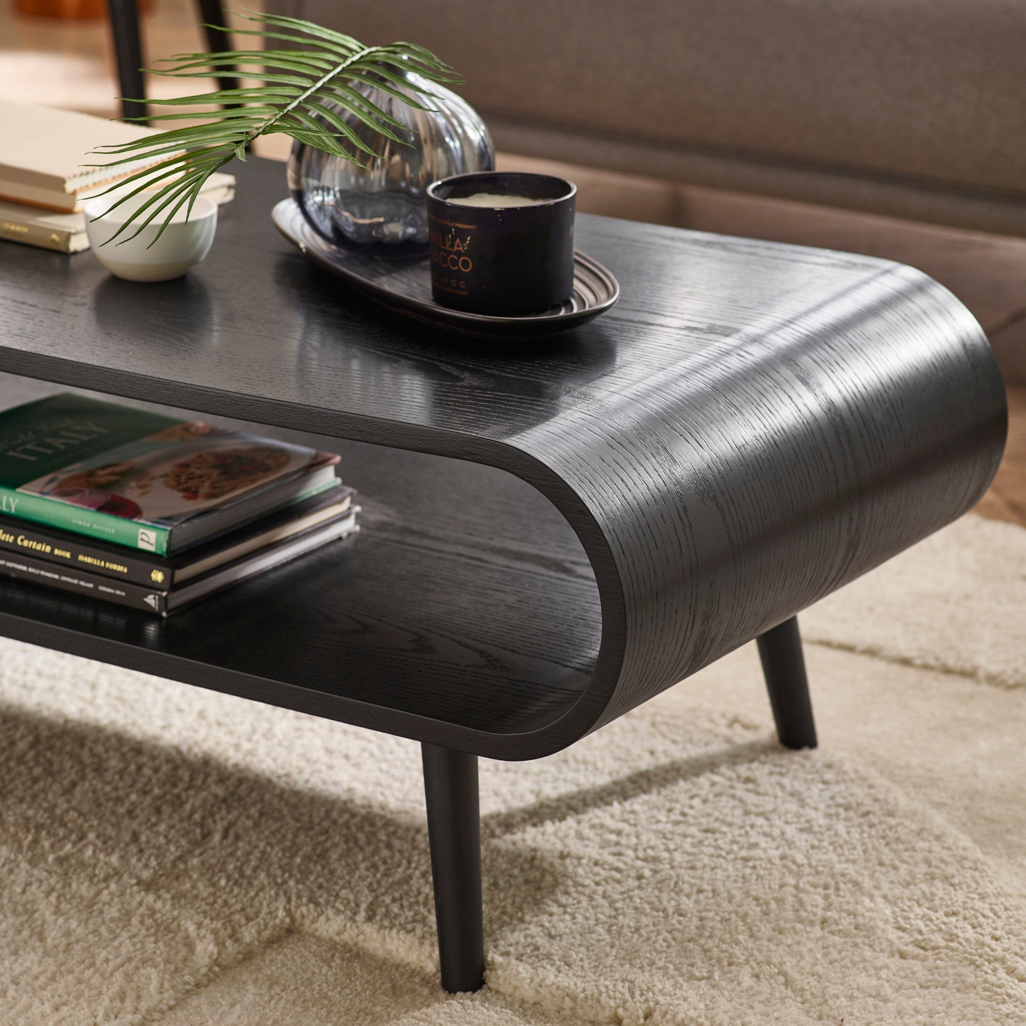 Close-up of coffee table surface with decorative tray, glass vase, and candle on black wood