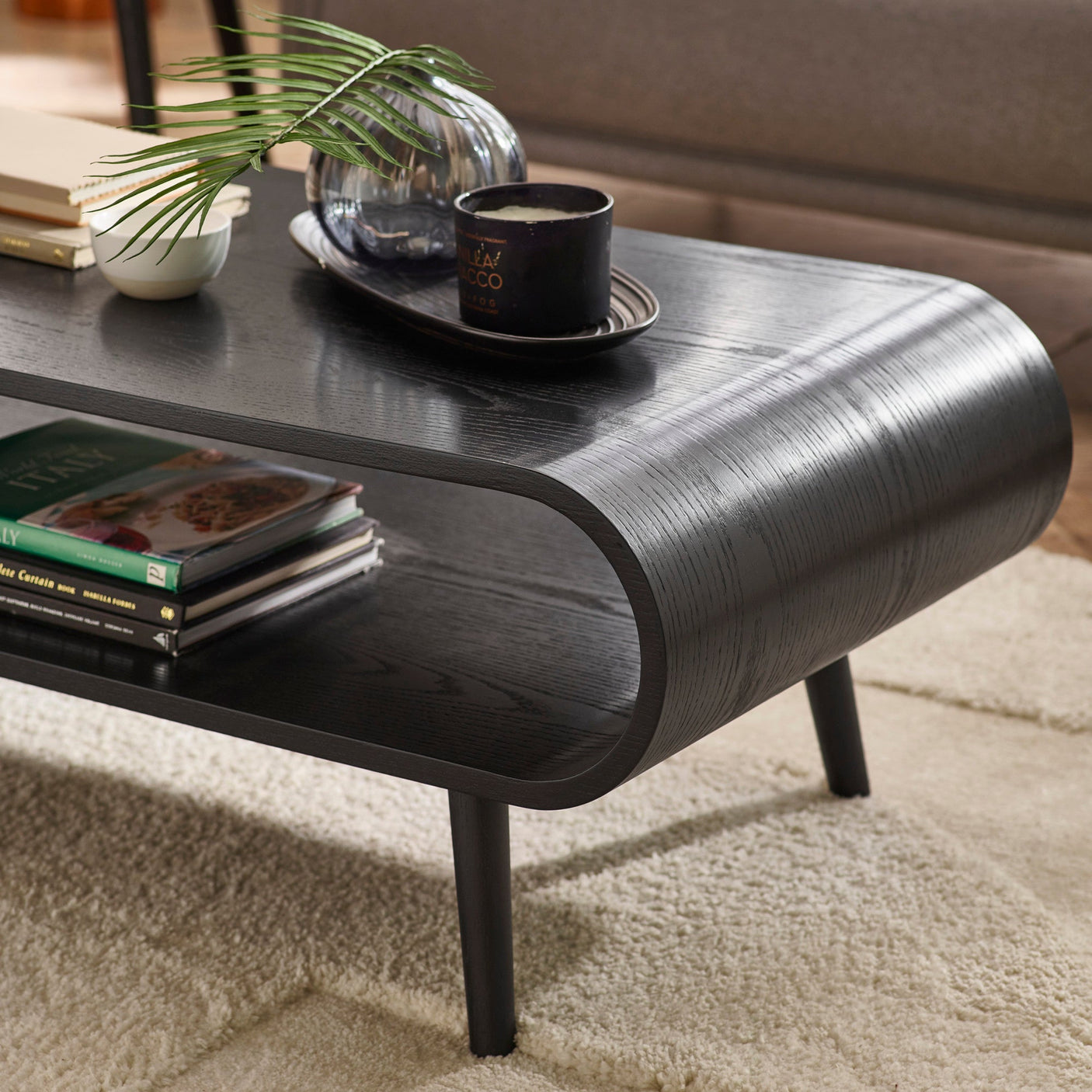 Close-up of coffee table surface with decorative tray, glass vase, and candle on black wood