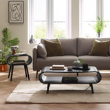 Black wood coffee table with rounded edges and tapered legs in a bright living room setting