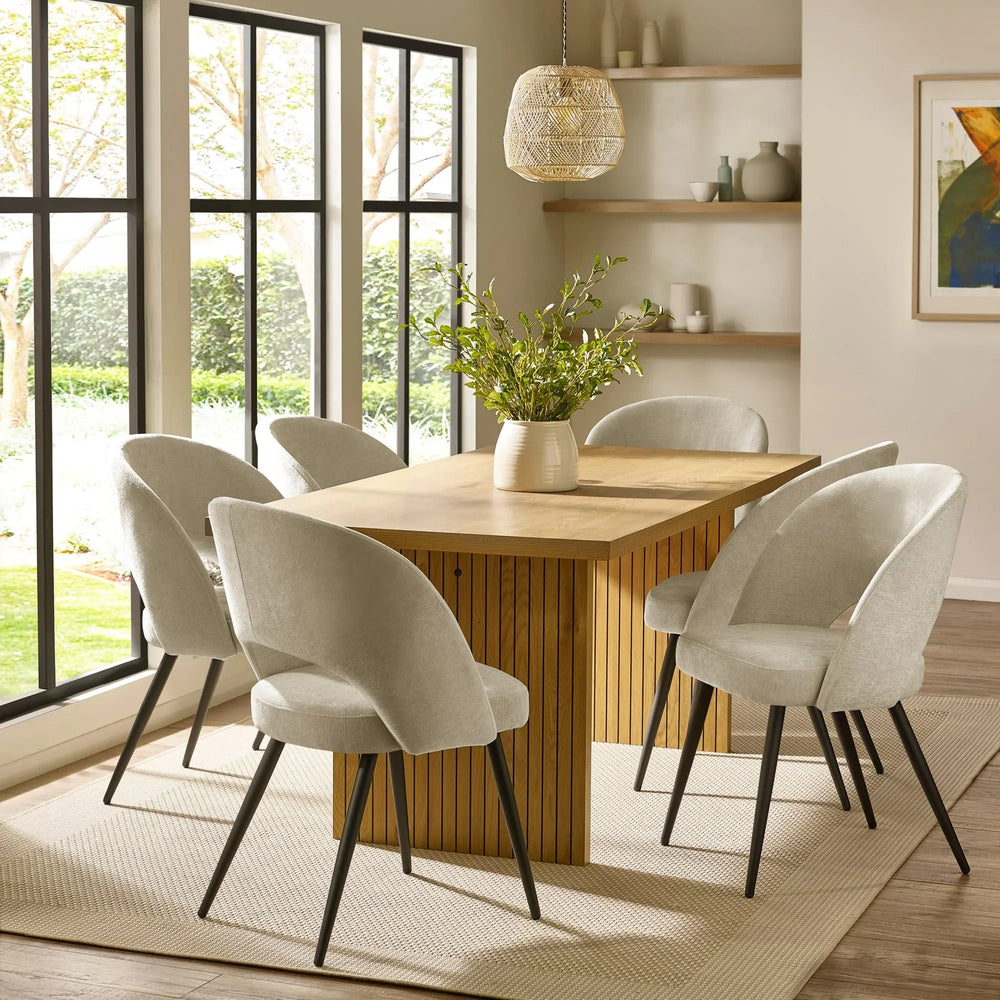 Modern wood dining table with six upholstered cream chairs in bright dining room