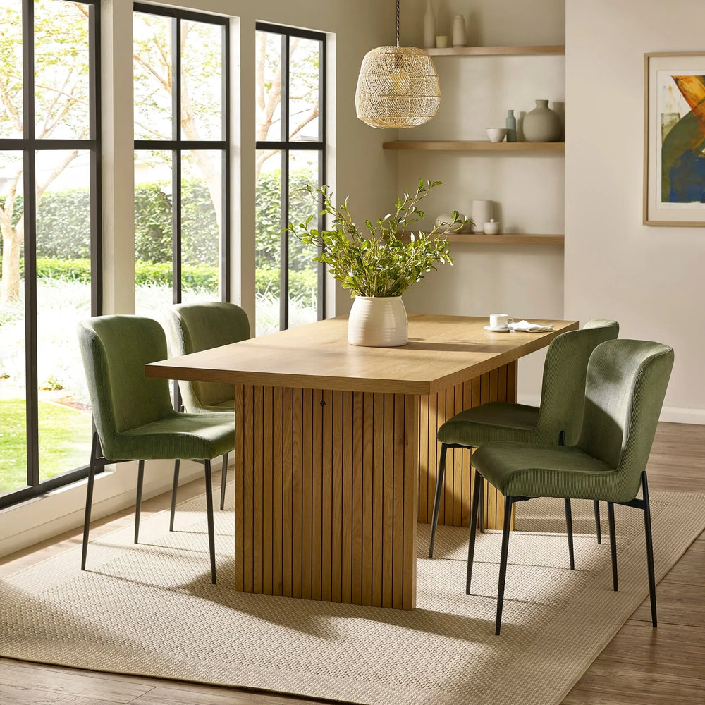 Modern wood dining table with green velvet chairs in a bright dining room setting
