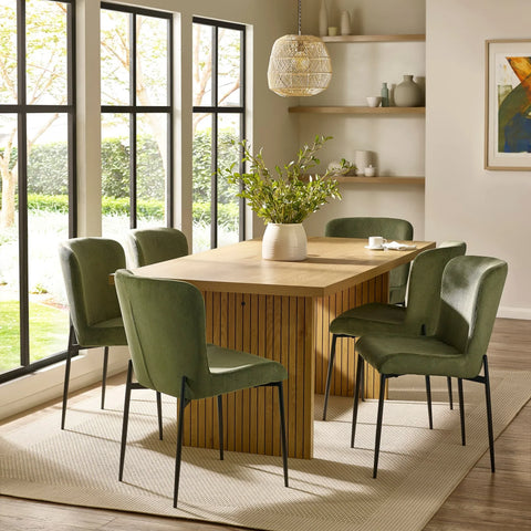 Oak dining table with green velvet chairs on beige rug in bright modern dining room