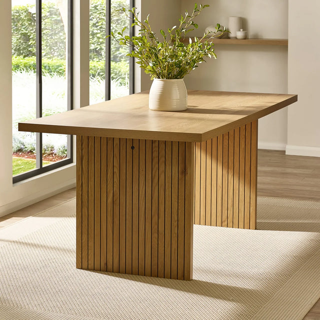 Rectangular oak dining table with slatted base and vase on beige rug near window