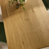 Oak dining table top with natural wood grain, green chair and plant decor visible