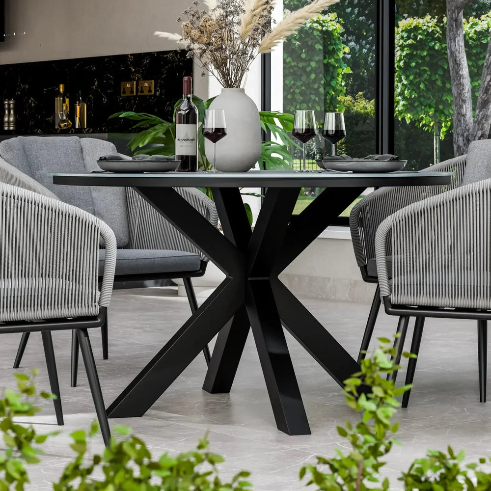 Modern black dining table with glass top, grey chairs, and decorative vase indoors