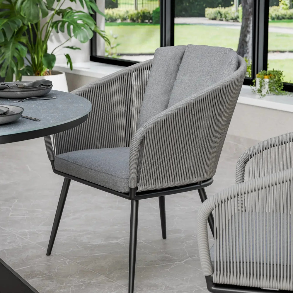 Grey rope dining chair with padded seat in modern dining area by window and plants