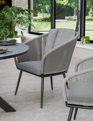 Grey rope dining chair with padded seat in modern dining area by window and plants