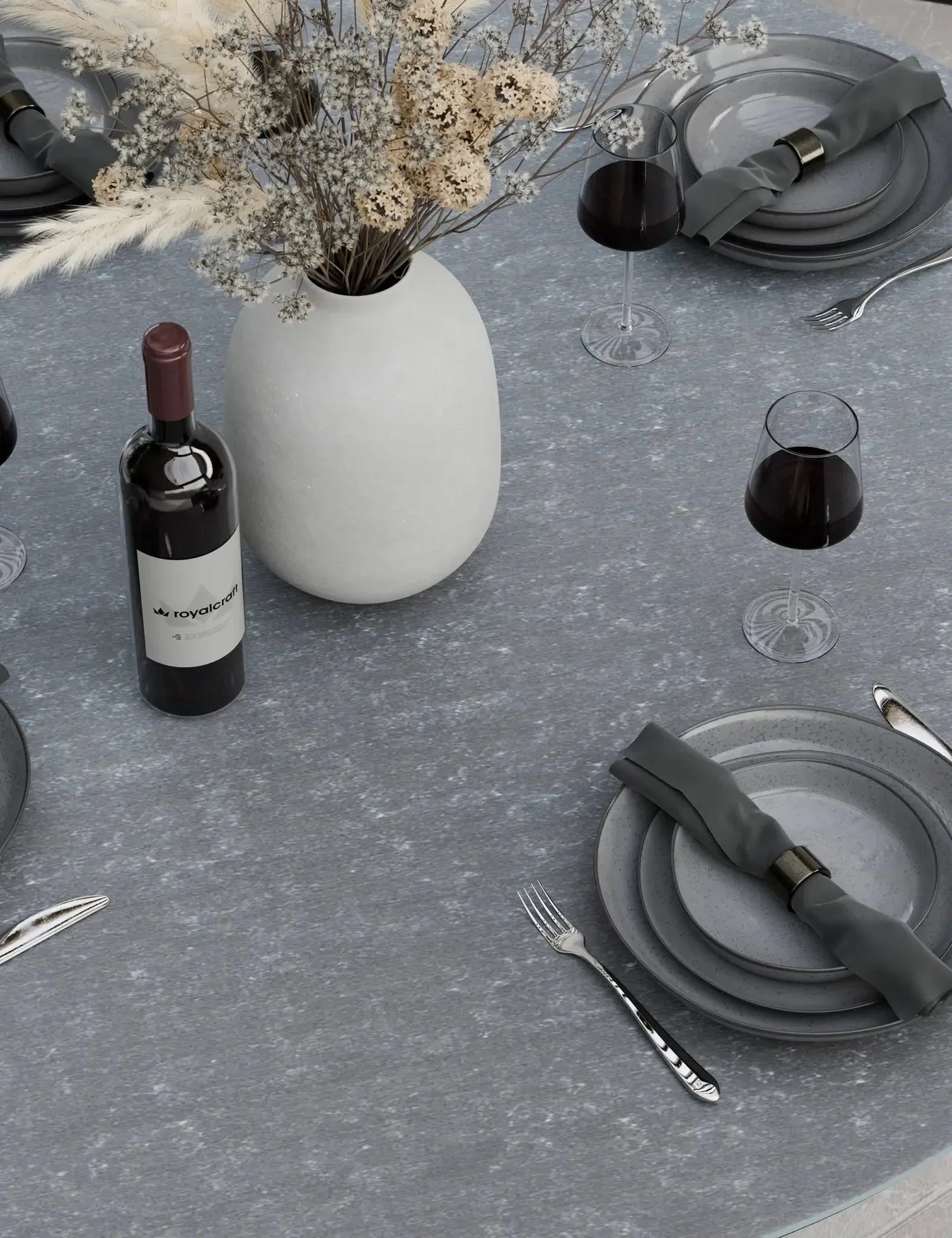 Round grey stone dining table set with plates, cutlery, wine glasses and white vase