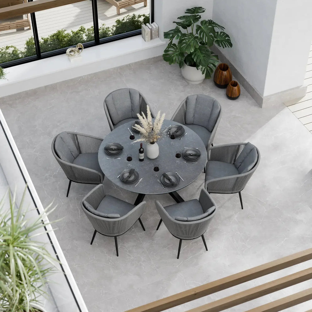 Round grey dining table set with six cushioned chairs in modern indoor setting