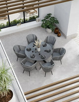 Round grey dining table set with six cushioned chairs in modern indoor setting