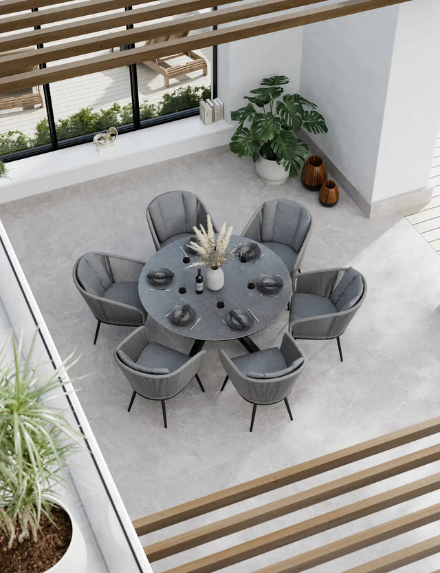 Round grey dining table set with six cushioned chairs in modern indoor setting