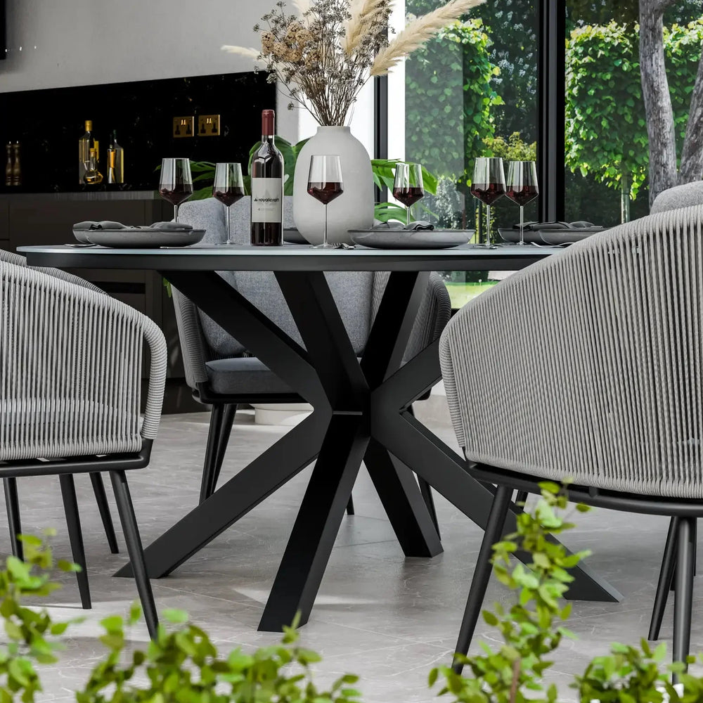 Modern black dining table with star-shaped base, grey chairs, and wine glasses in bright room