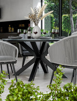 Modern black dining table with star-shaped base, grey chairs, and wine glasses in bright room
