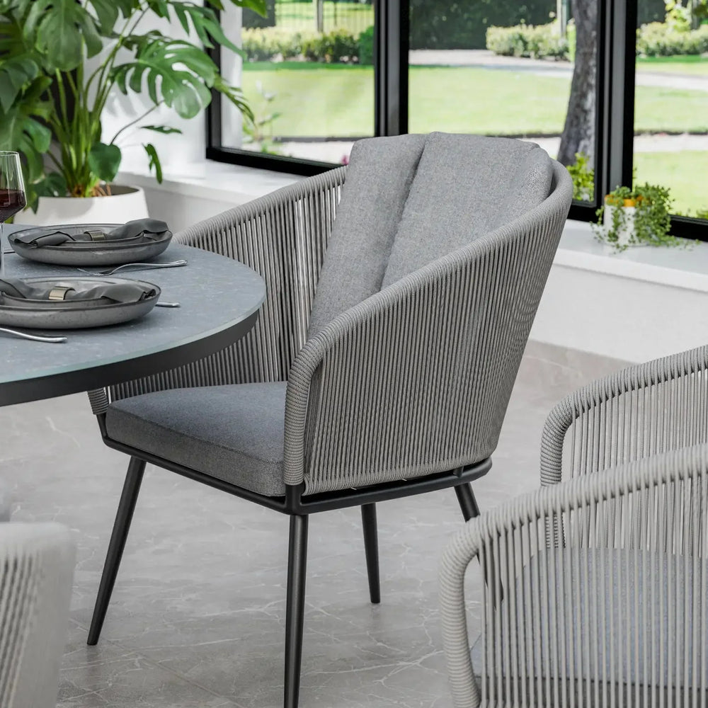 Grey rope dining chair with cushioned seat and backrest near round dining table