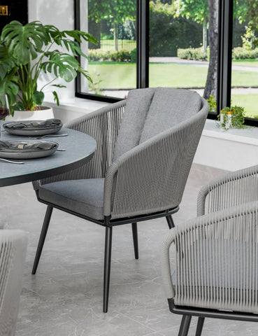 Grey rope dining chair with cushioned seat and backrest near round dining table