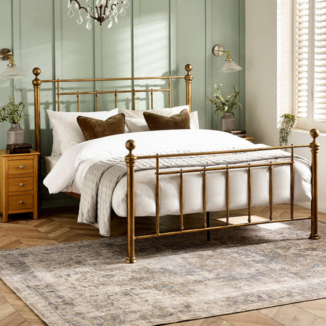 Gold metal bed with vertical spindles, white bedding, brown pillows, wooden bedside tables, and green paneled wall