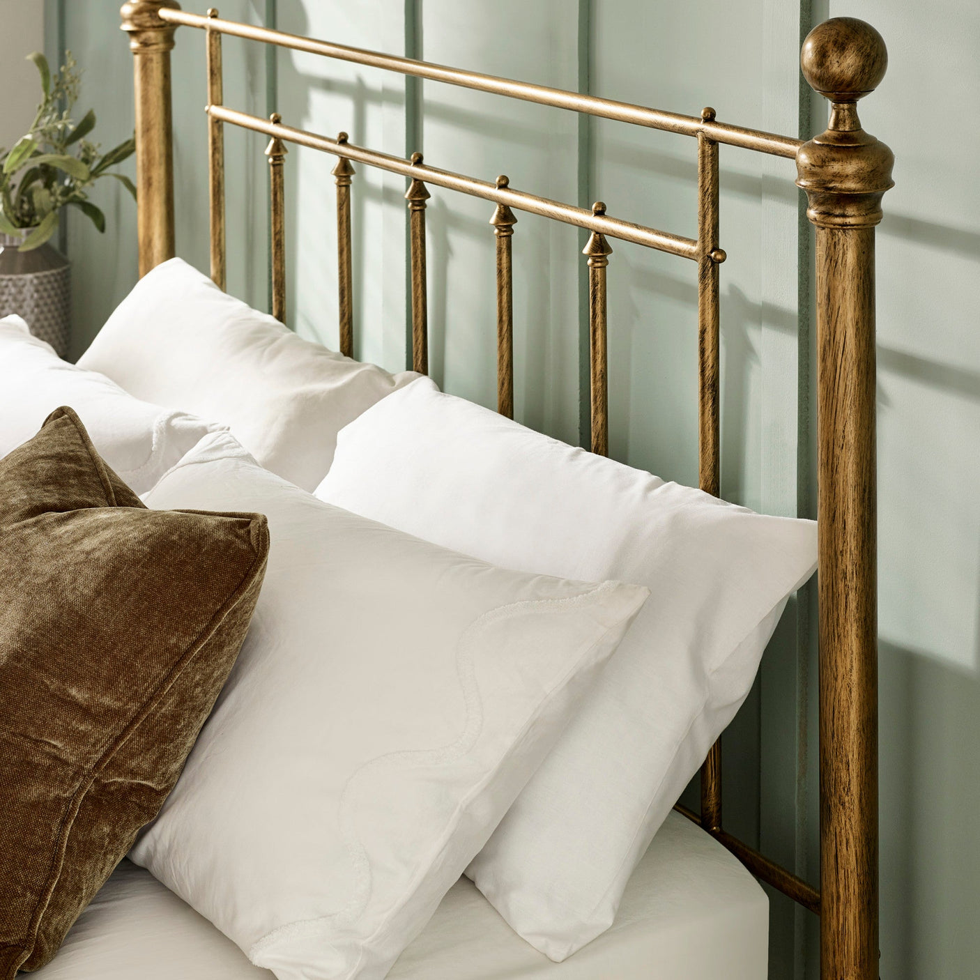 Close-up of brass metal headboard with vertical bars, finials, white pillows and brown cushion.