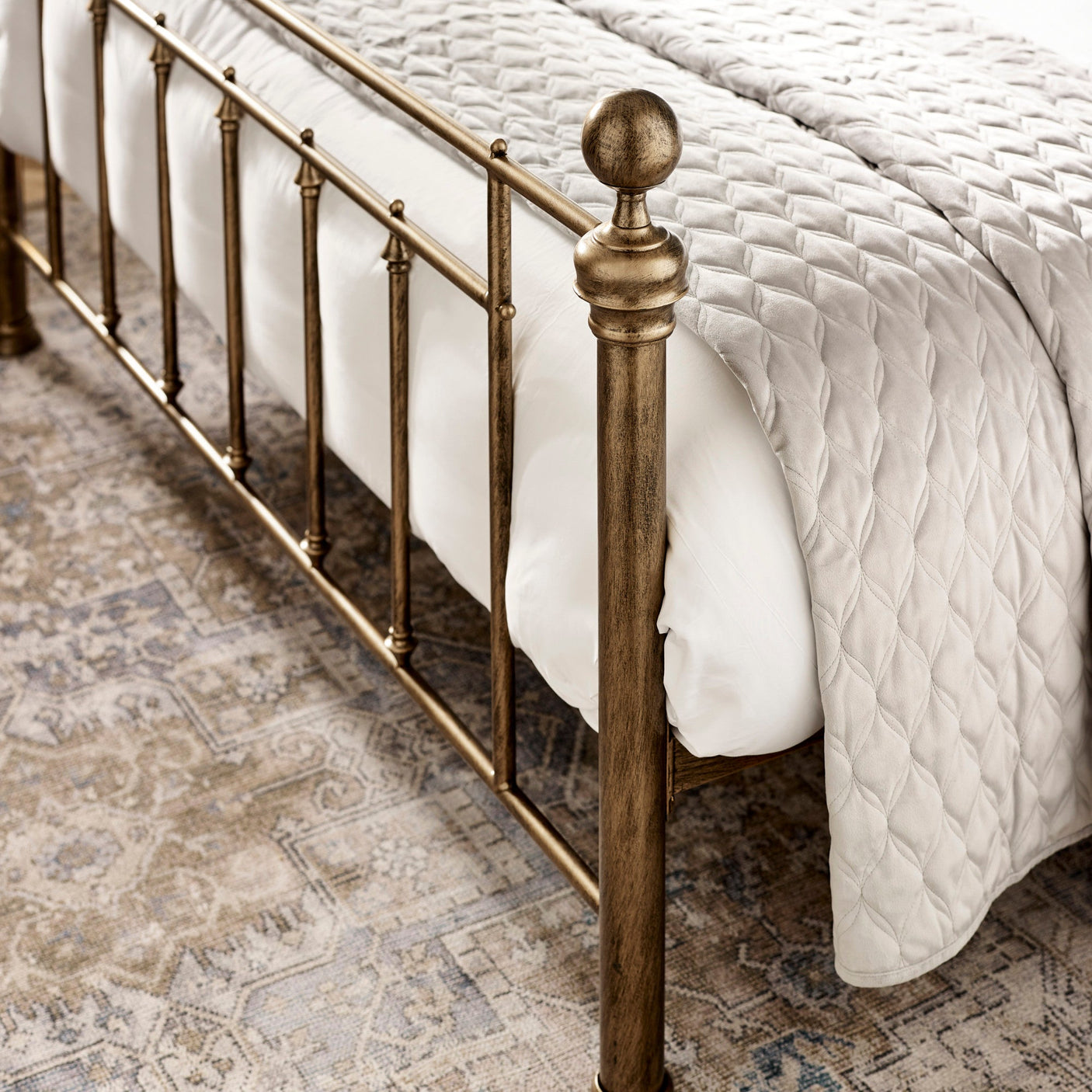 Close-up of brass metal footboard with vertical bars and rounded finials, styled with white quilt.