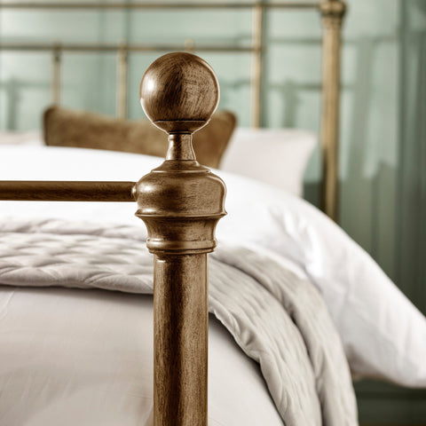 Detailed close-up of rounded finial on brass metal bedpost with bedding in soft focus.