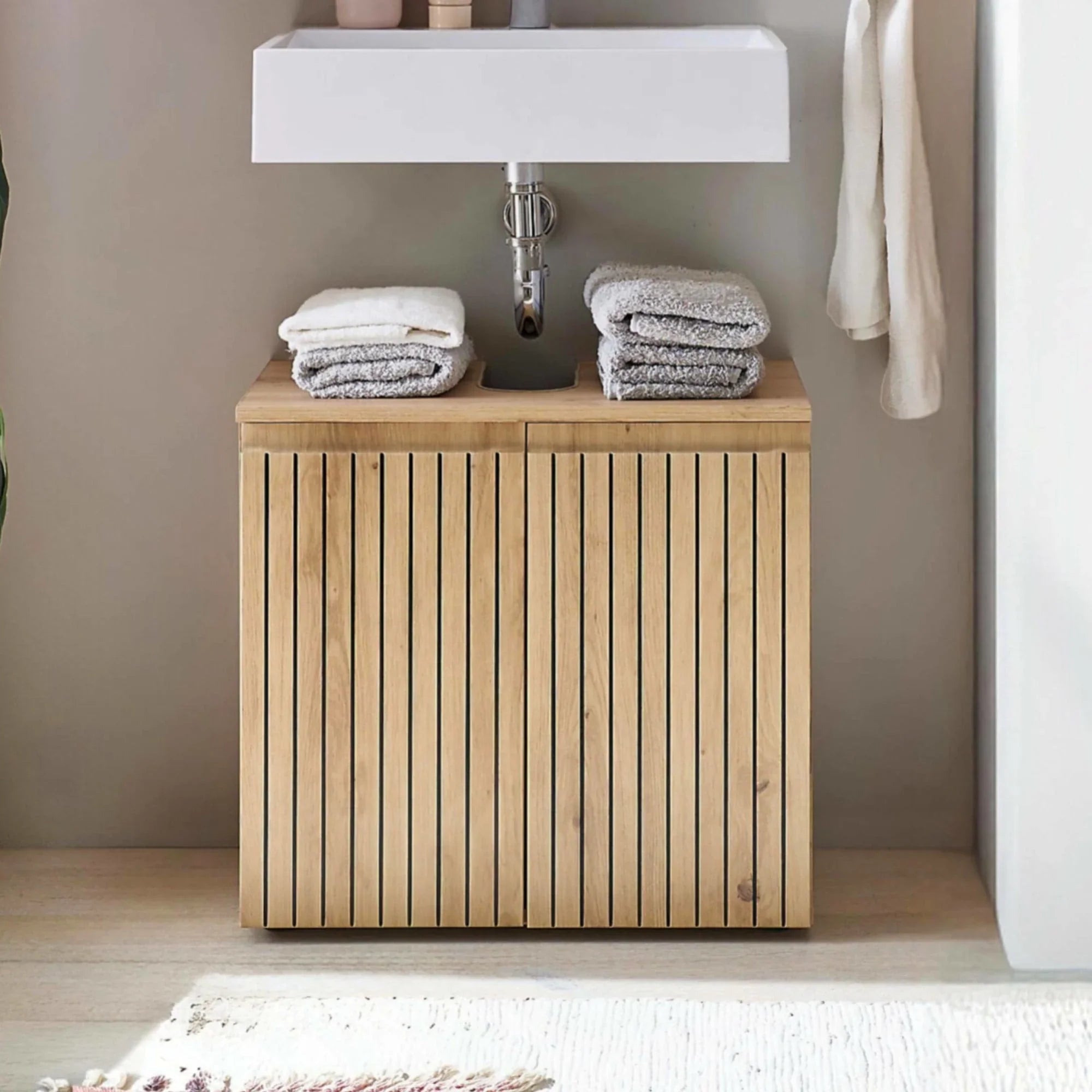 Wooden bathroom vanity unit with vertical slats under sink, folded towels on top
