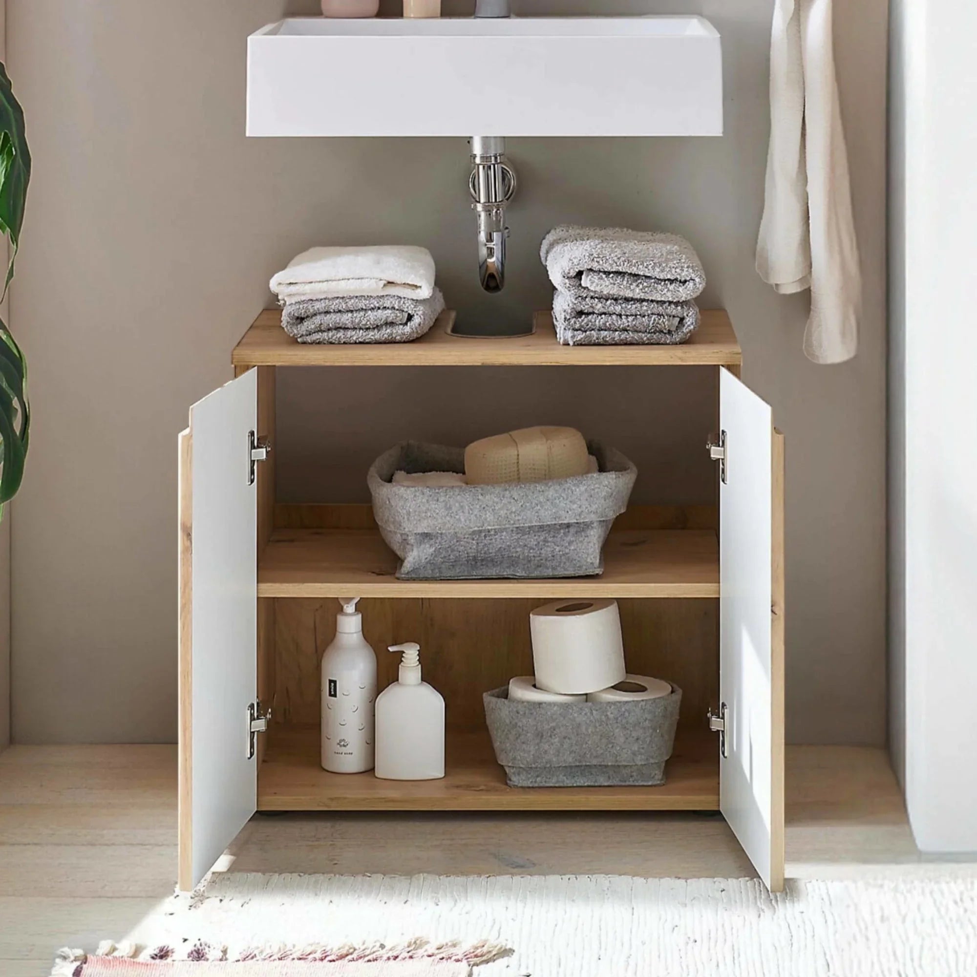 Wood and white bathroom storage cabinet under sink with towels baskets and toiletries