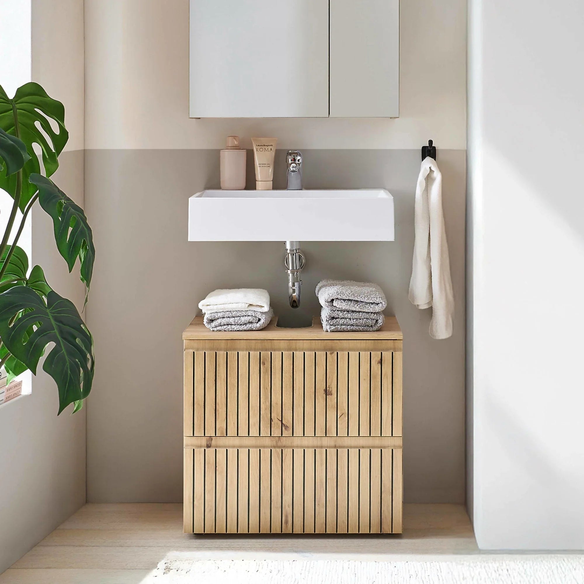 Wooden bathroom vanity unit with slatted doors below white basin and stacked towels