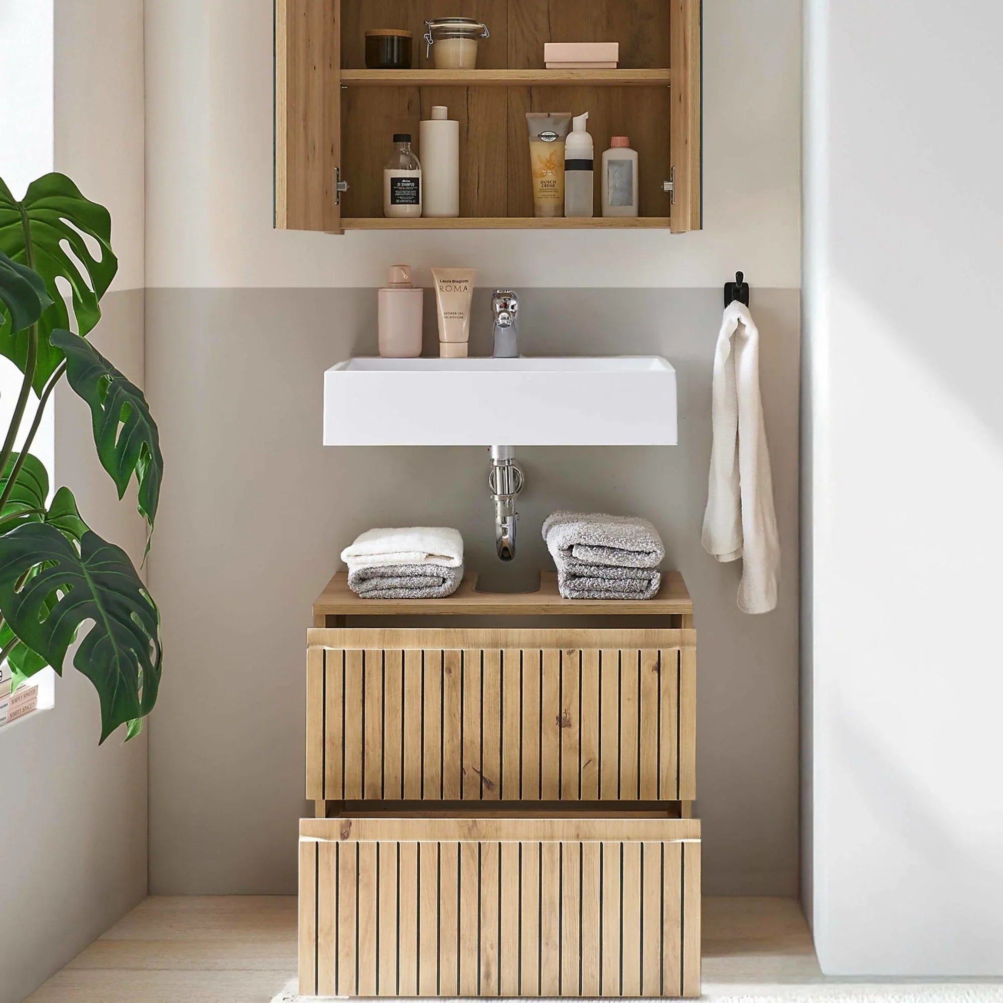 Wood bathroom vanity unit with open drawers, white sink, and folded towels in modern setting