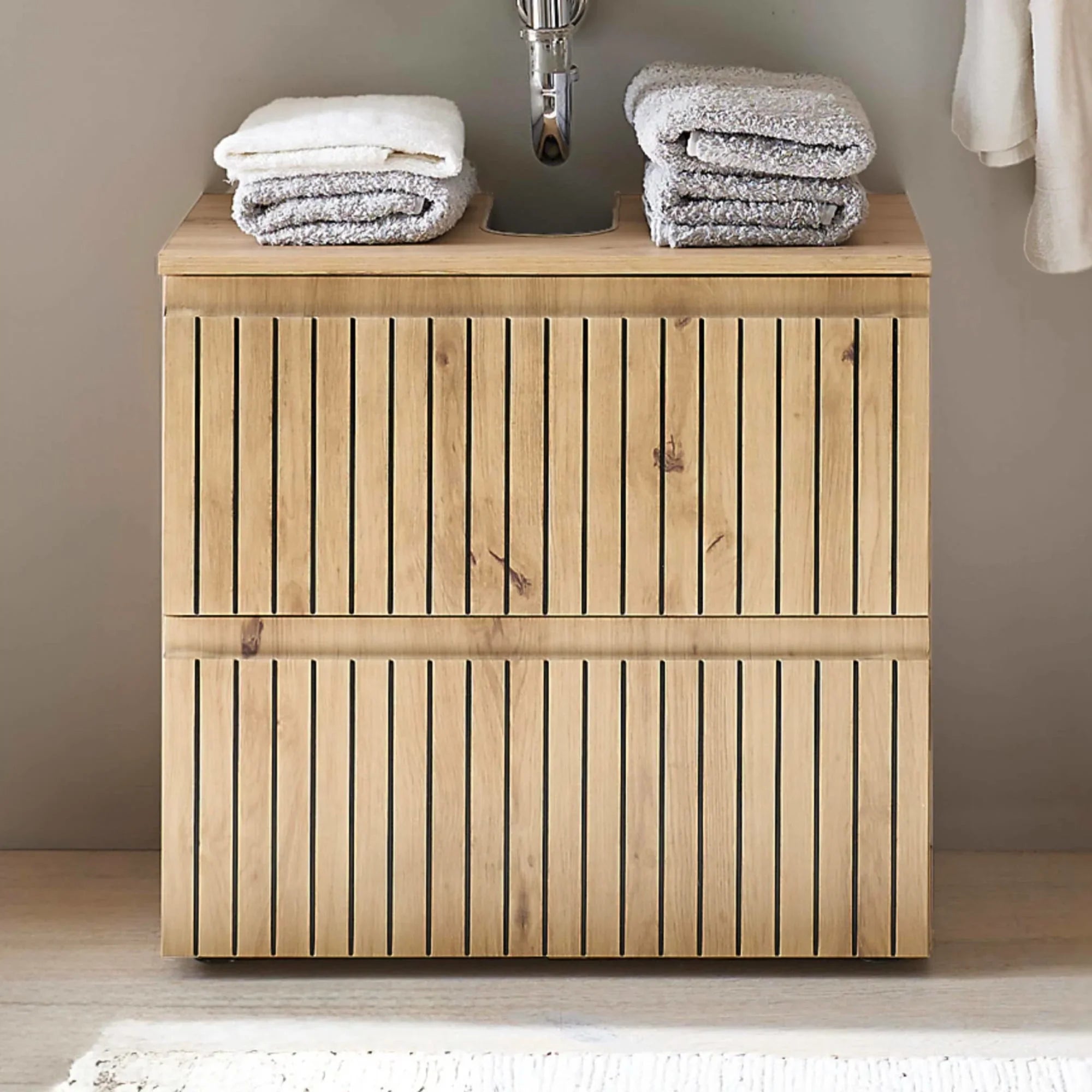 Wood slatted bathroom vanity unit with towels stacked on top under a wall-mounted sink