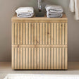 Wood slatted bathroom vanity unit with towels stacked on top under a wall-mounted sink