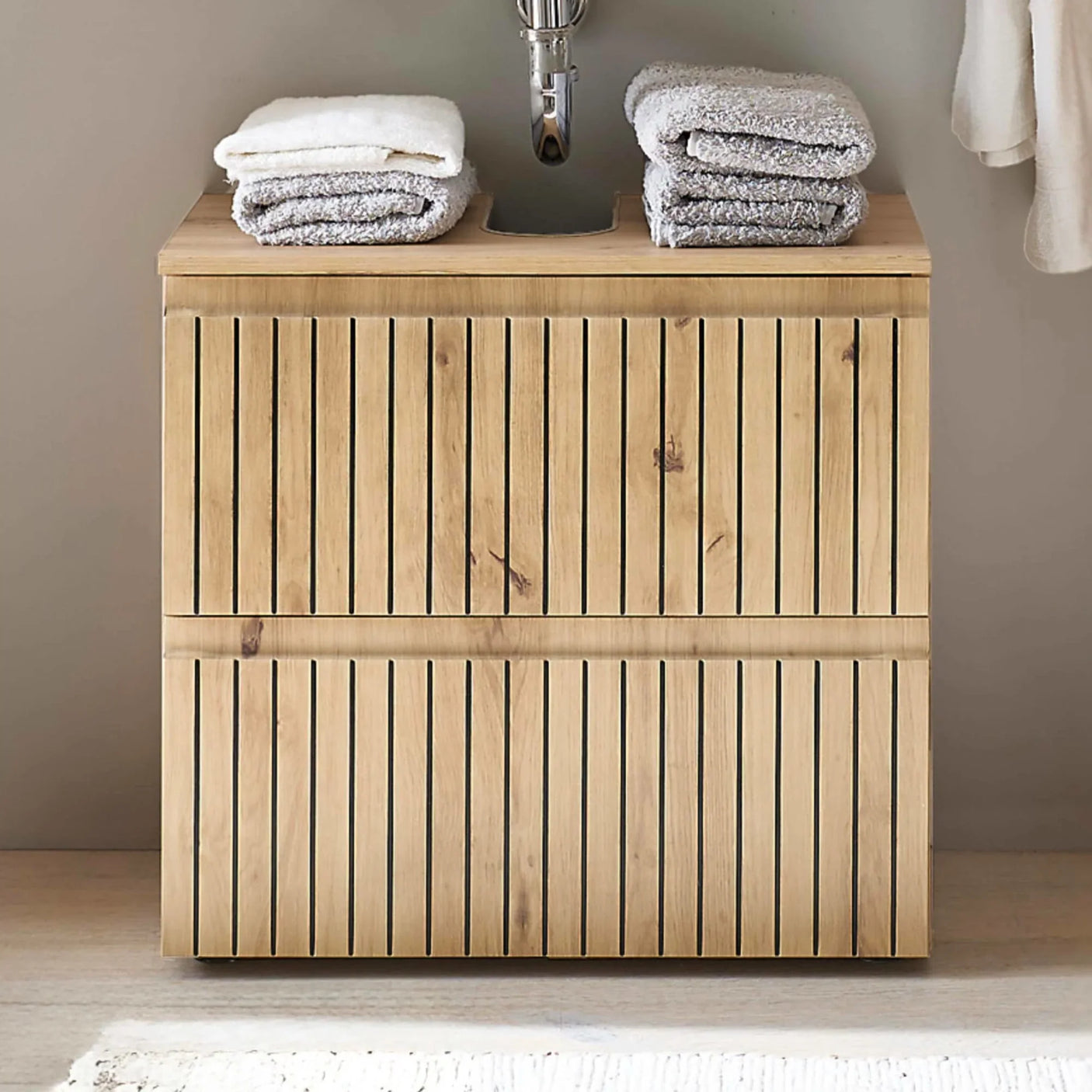 Wood slatted bathroom vanity unit with towels stacked on top under a wall-mounted sink