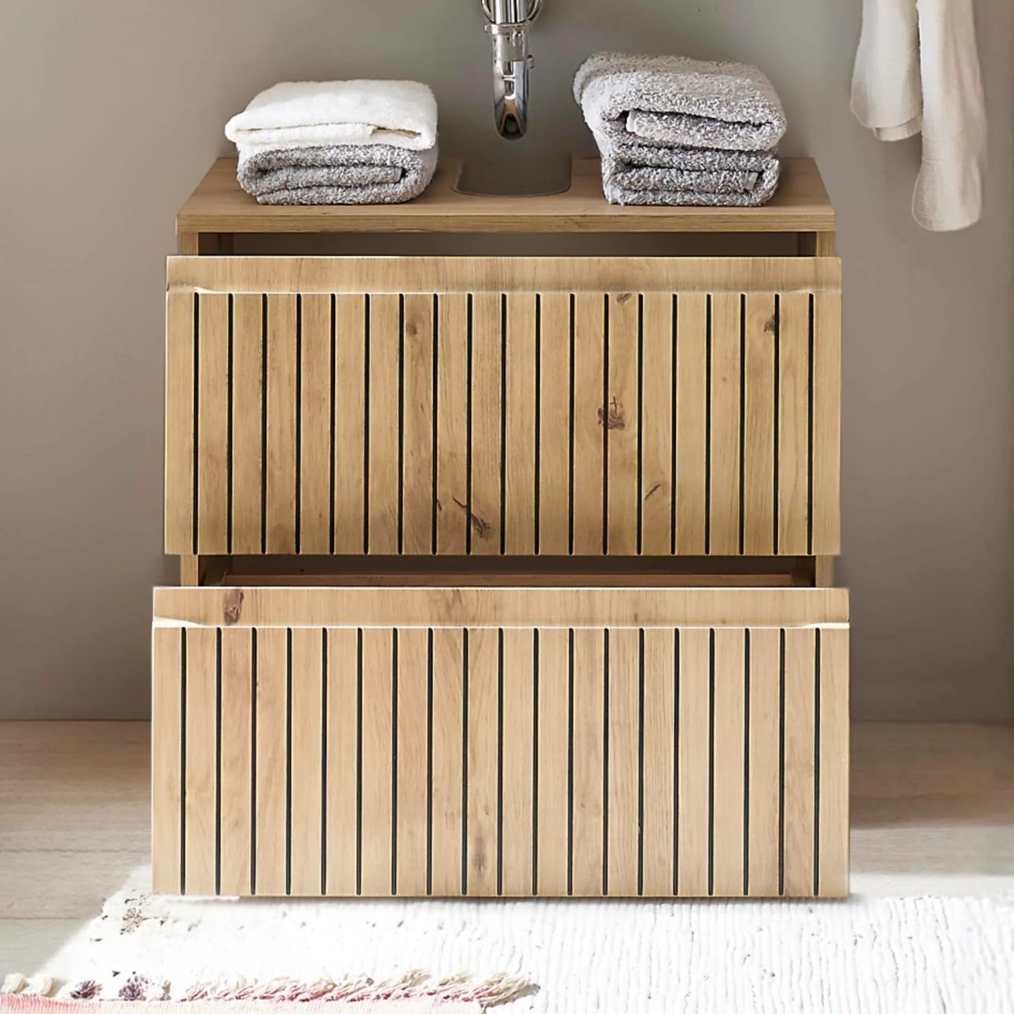 Wooden bathroom vanity unit with two drawers and stacked folded towels on top