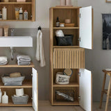 Tall oak bathroom storage cabinet with white doors and open shelves, filled with towels