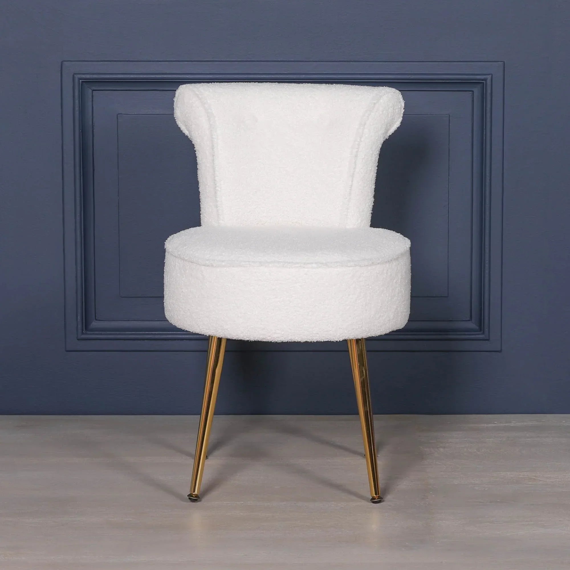 White accent chair with gold metal legs against navy blue wall on light wood floor