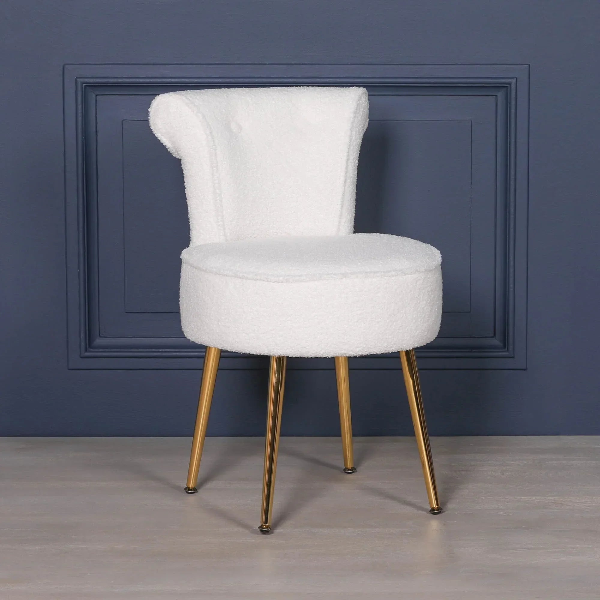 White boucle accent chair with gold metal legs against navy wall panel background