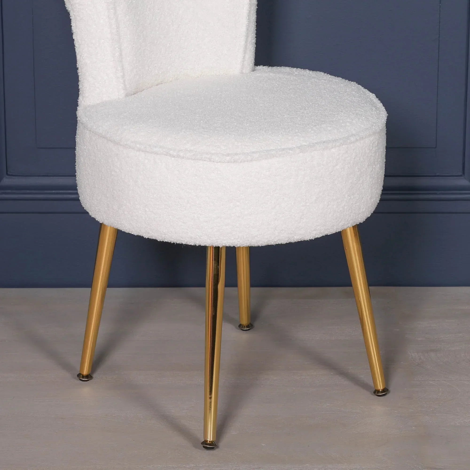White boucle accent chair with gold metal legs against dark blue wall
