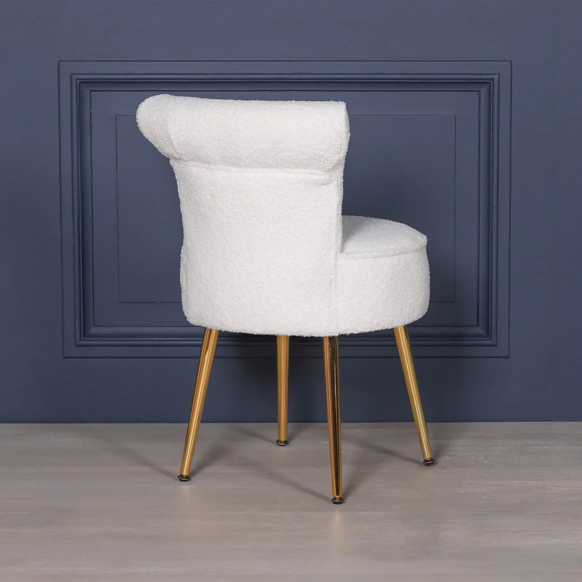 White boucle accent chair with gold metal legs against navy blue wall