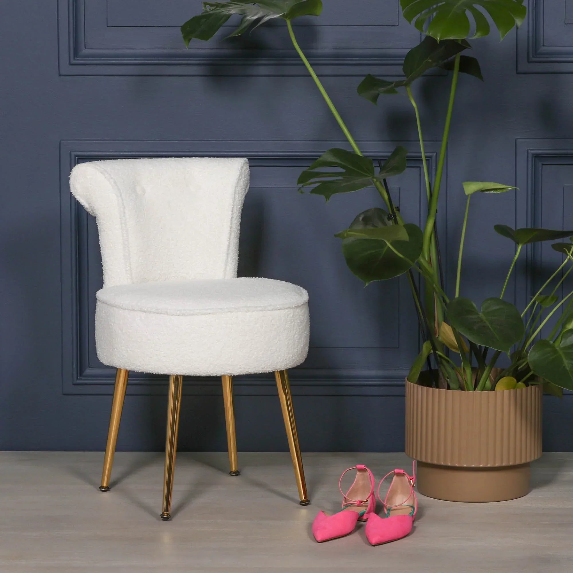 White boucle accent chair with gold legs beside potted plant and pink shoes on wood floor