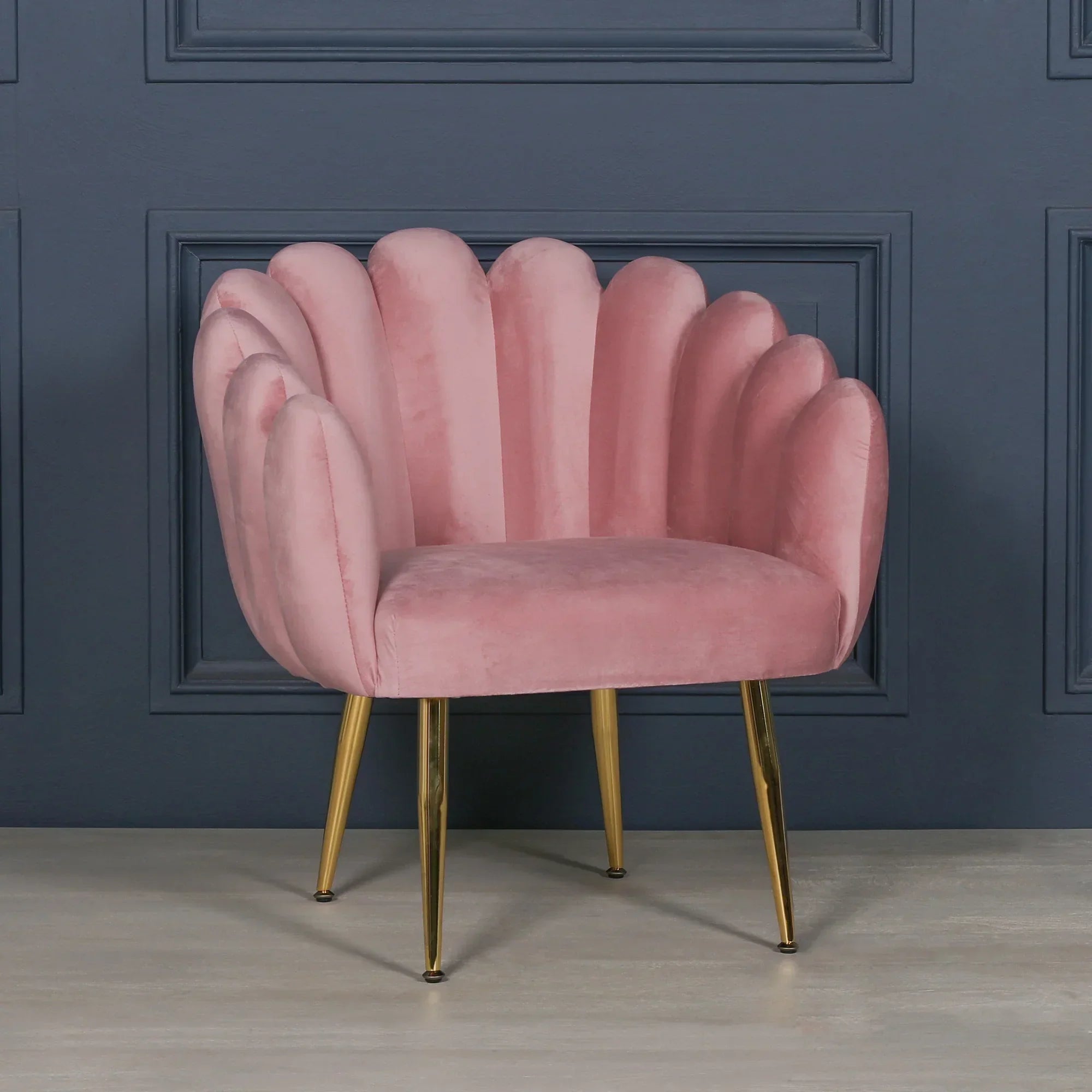 Pink velvet accent chair with scalloped back and gold legs against dark panel wall
