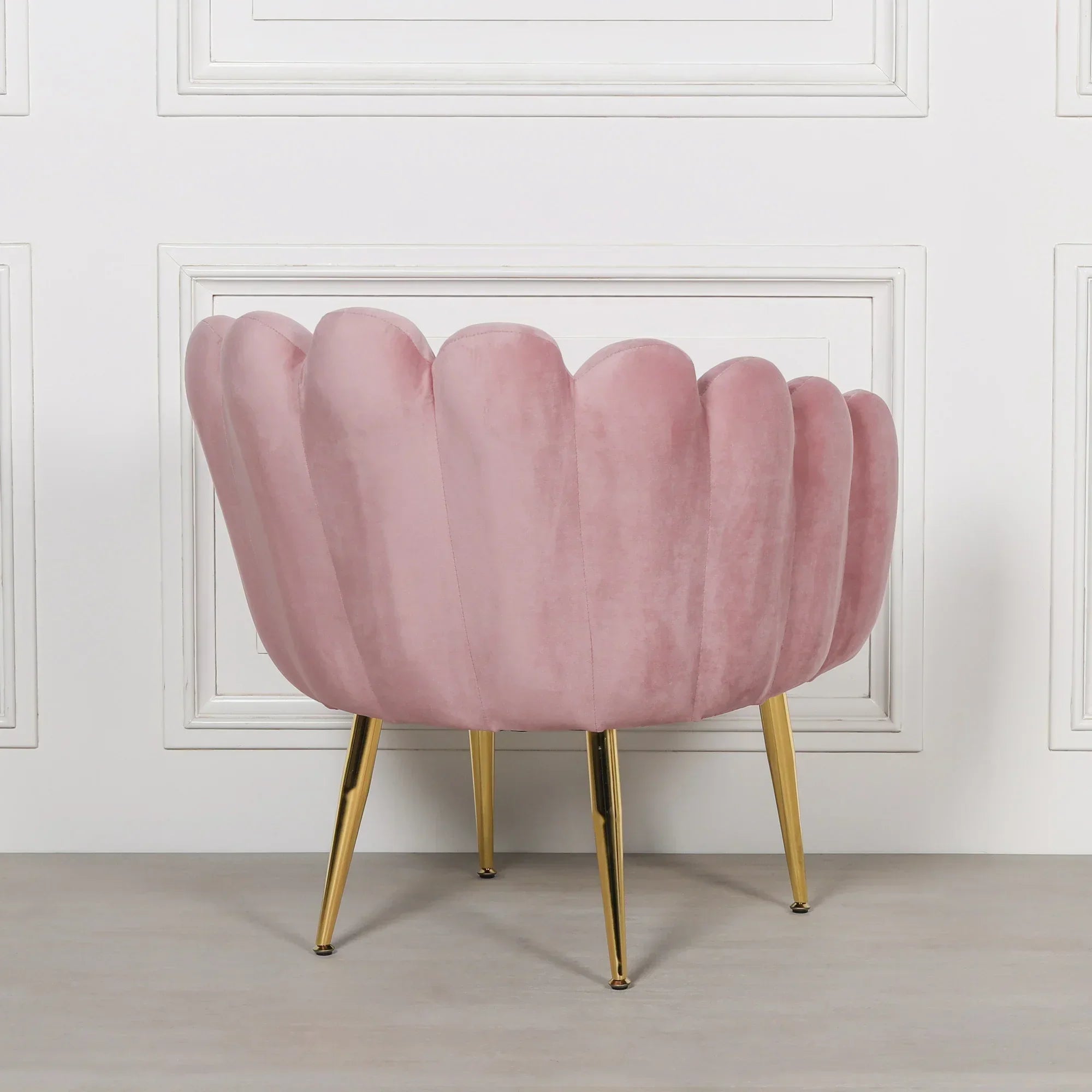 Pink velvet accent chair with scalloped back and gold metal legs facing wall