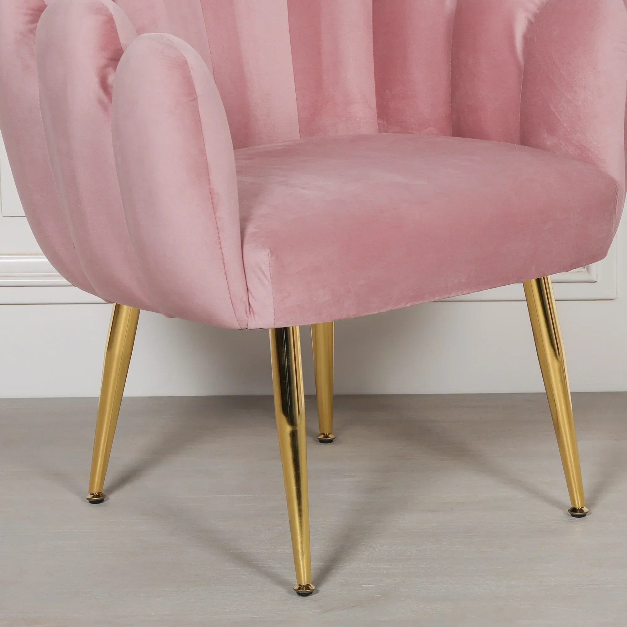 Pink velvet accent chair with gold metal legs against light flooring and wall panel