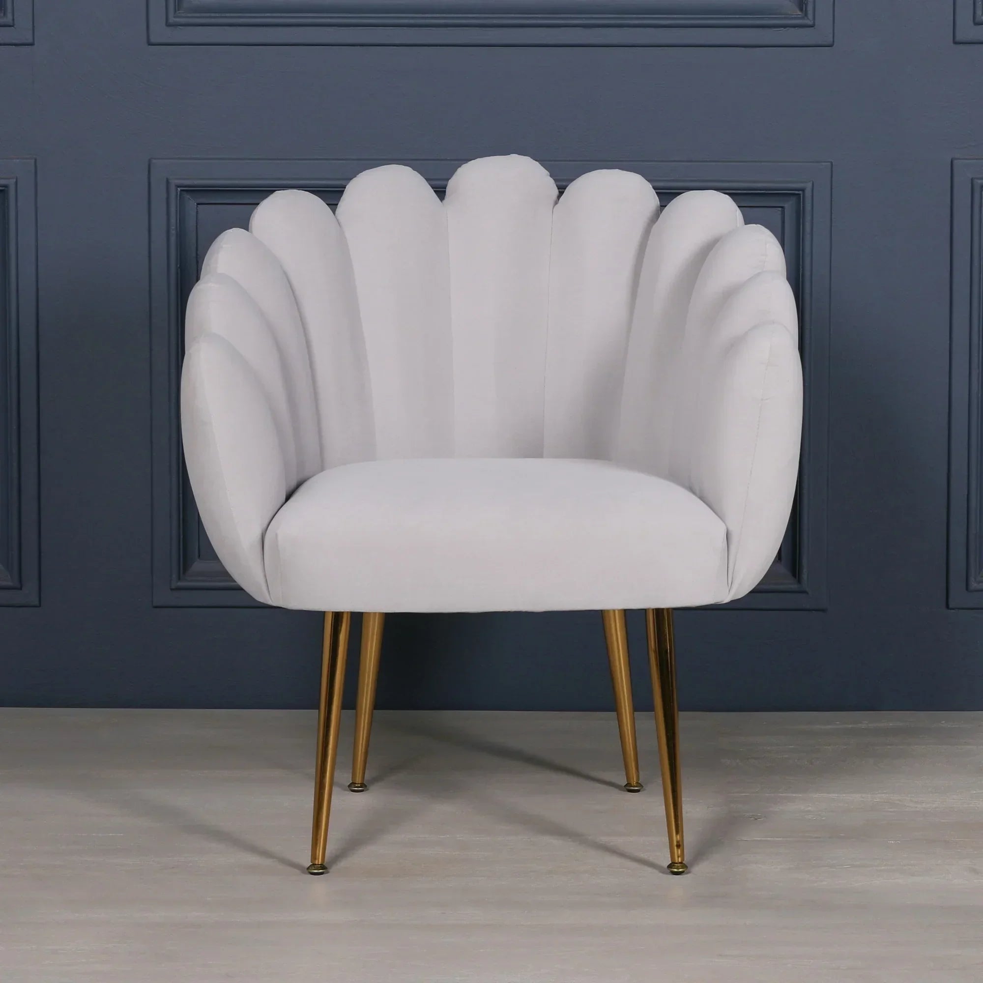 Grey accent chair with scalloped velvet backrest and gold metal legs against blue panel wall