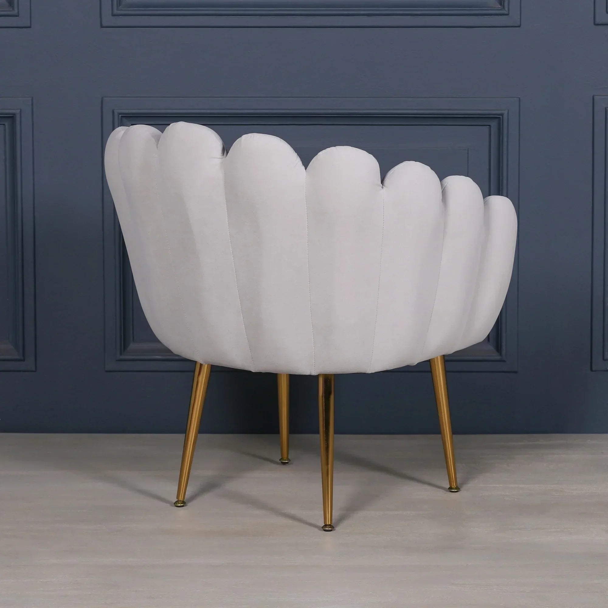 Scalloped white accent chair with gold metal legs against navy paneled wall