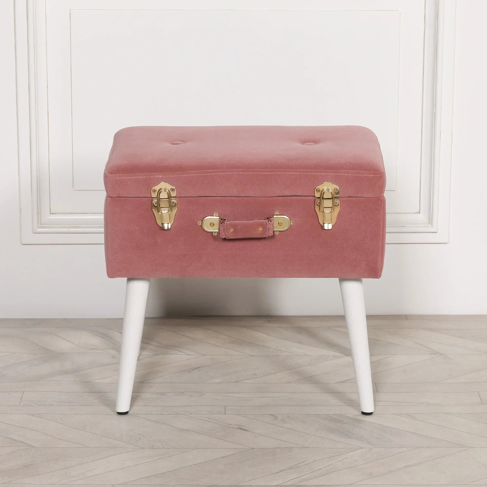Pink velvet storage bench with gold clasps and white legs on wooden floor